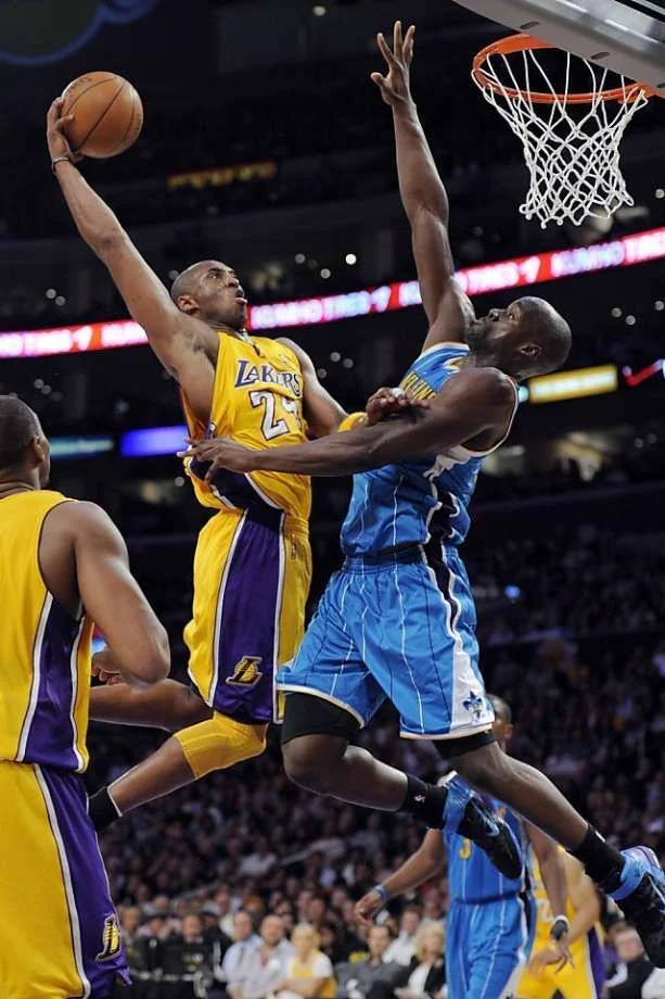 A basketball player in a yellow number 24 jersey reaching toward the hoop over a defender.